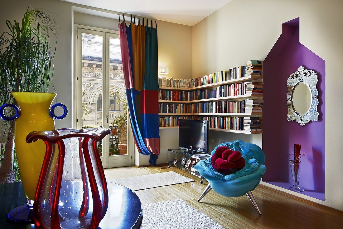 Modern living room with postmodern highlights - blue plush armchair in front of purple niche and colourful glass vases on table