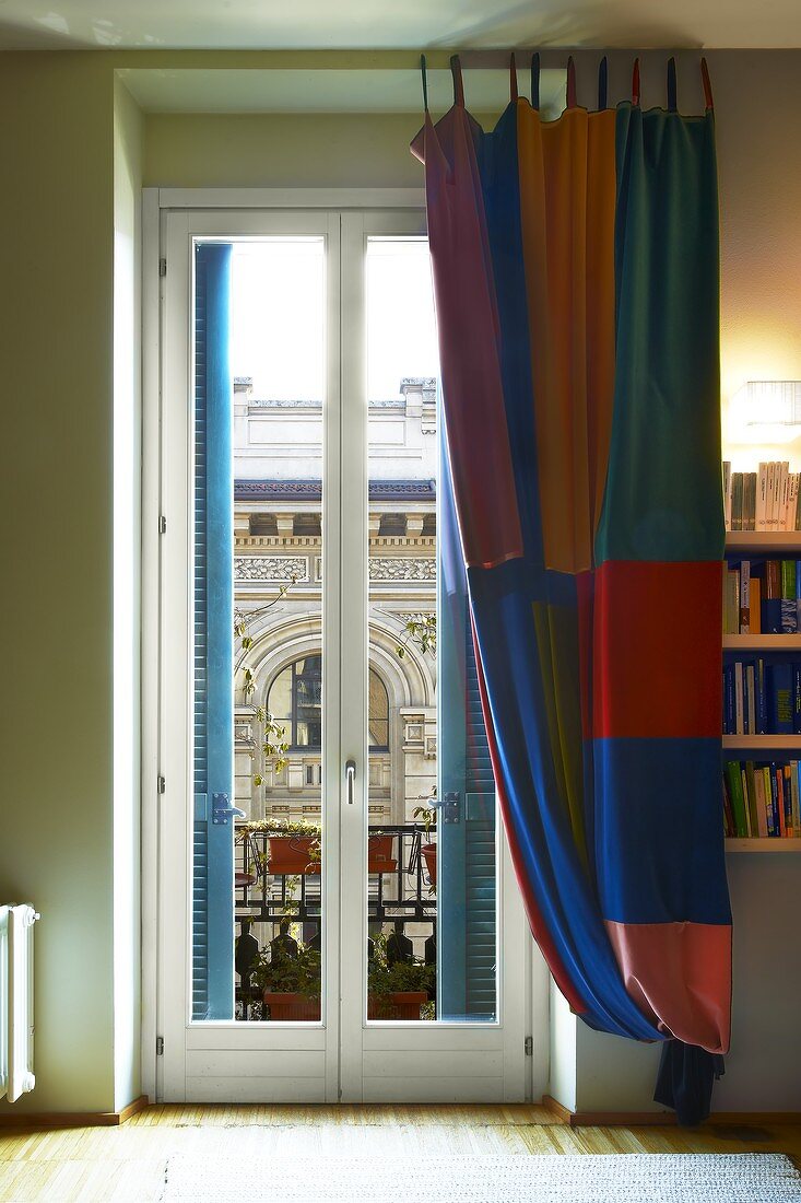 Bodenlanger Vorhang mit farbigem Karomuster vor der Balkontür und Blick auf historische Architektur