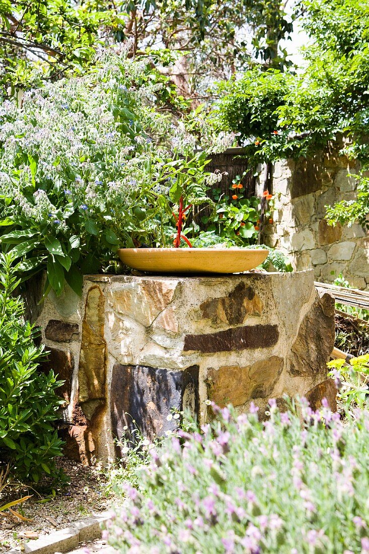 Vogelbecken auf Natursteinblock in mediterranem Garten