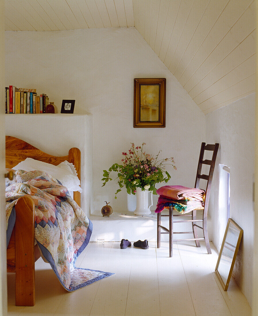 Wooden bed with patterned ceiling, bouquet of flowers and wooden floor in the attic room