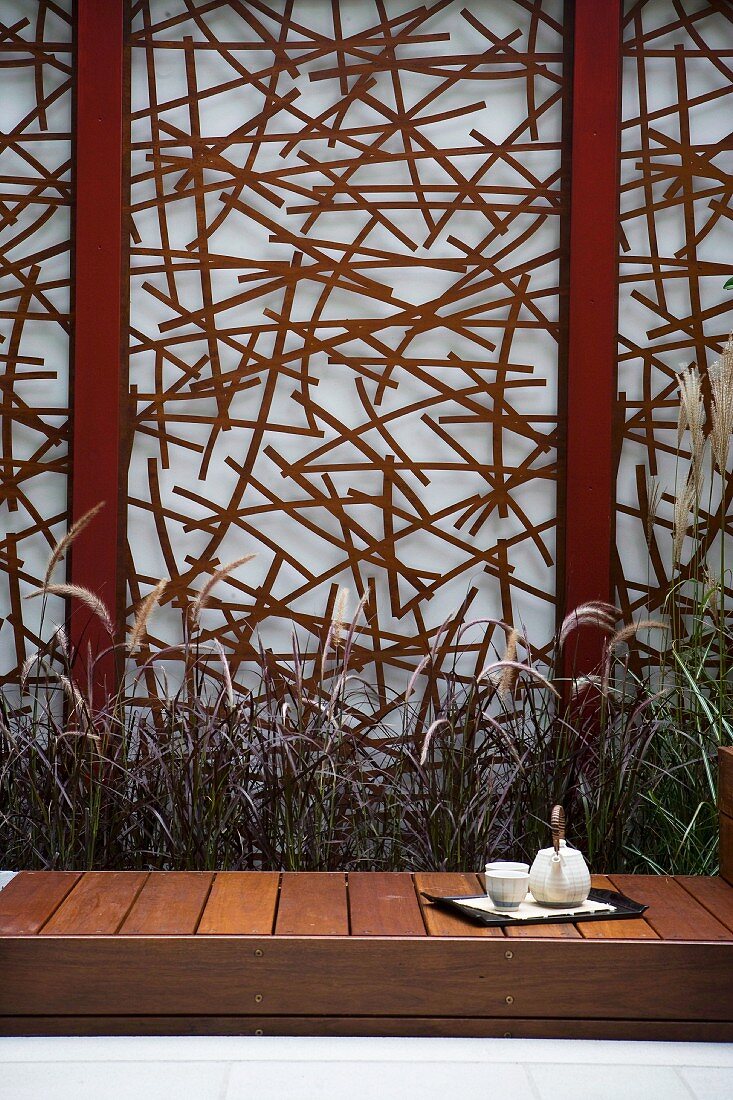 Afternoon tea in courtyard garden - purist wooden bench in front of artistic screen