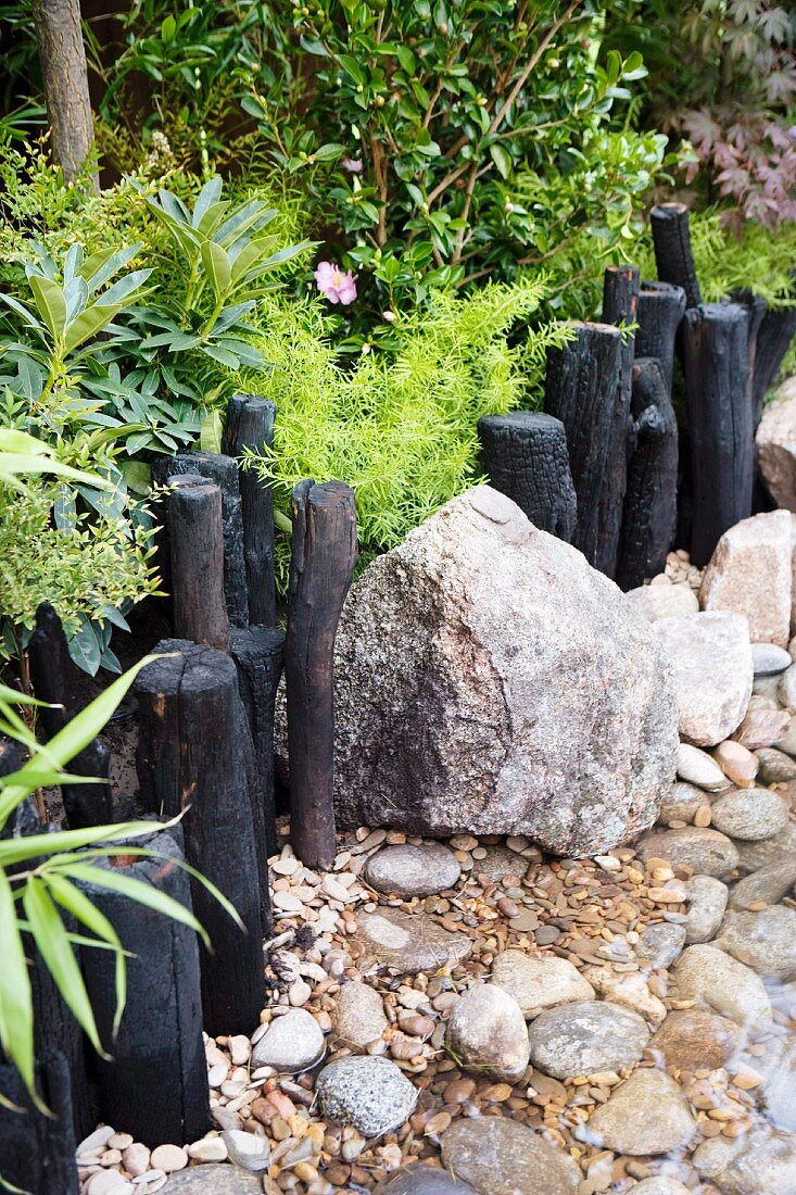 Decorative path border of black, carbonised wooden posts and boulders in garden