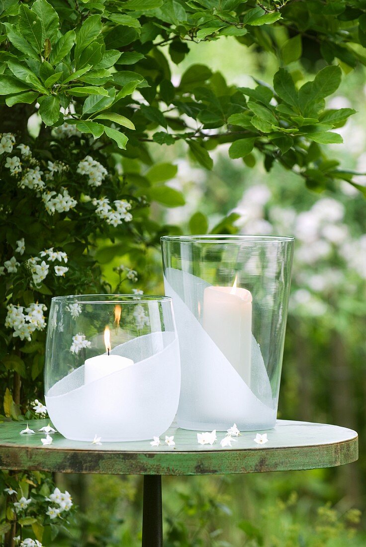 Two large candle lanterns on round metal table in garden