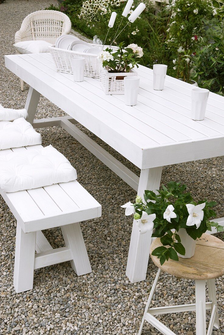 White garden table and matching bench decorated with flowers and set with porcelain crockery