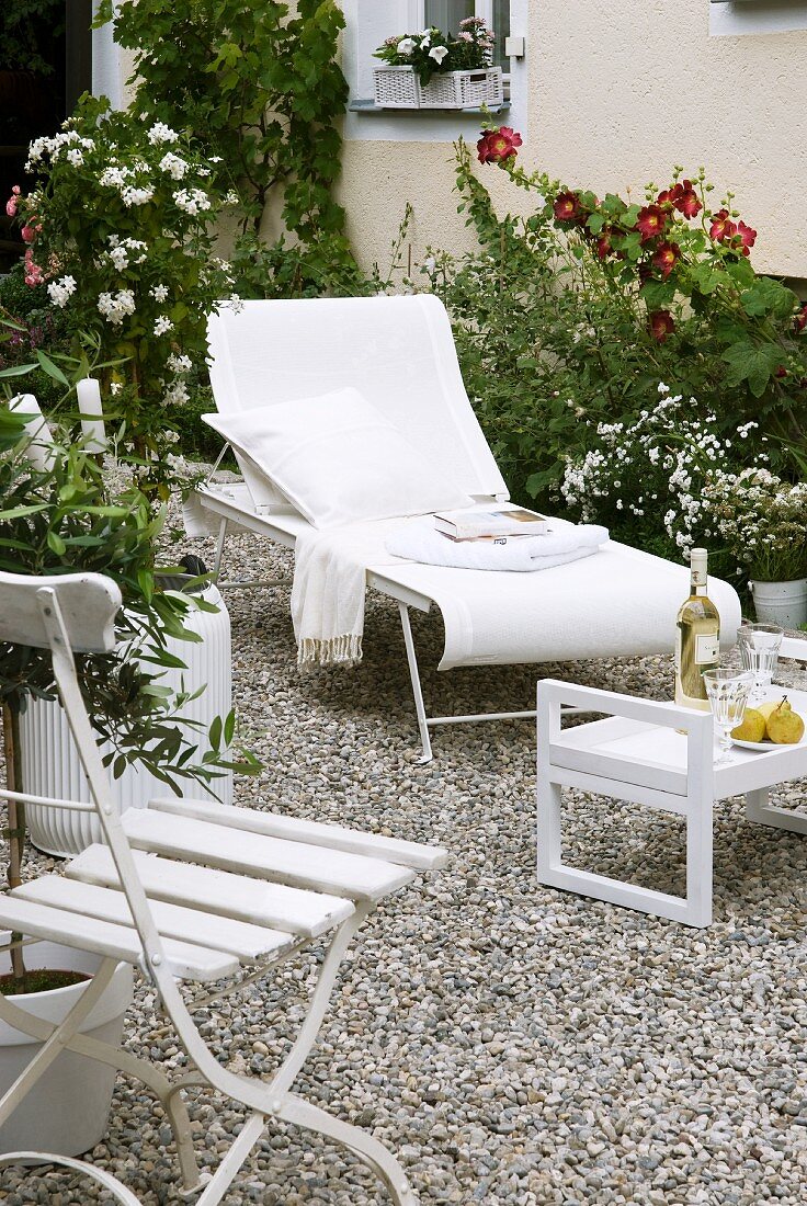 Sonnenliege, Klappstuhl und Tablett-Tisch in Weiß auf Kiesfläche im Garten