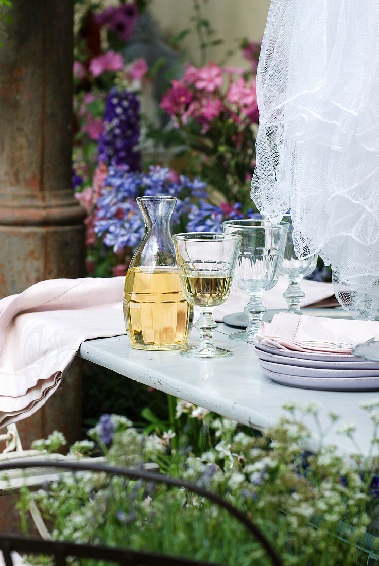 Rustic French wine decanter, glasses, plates and table linen on garden table