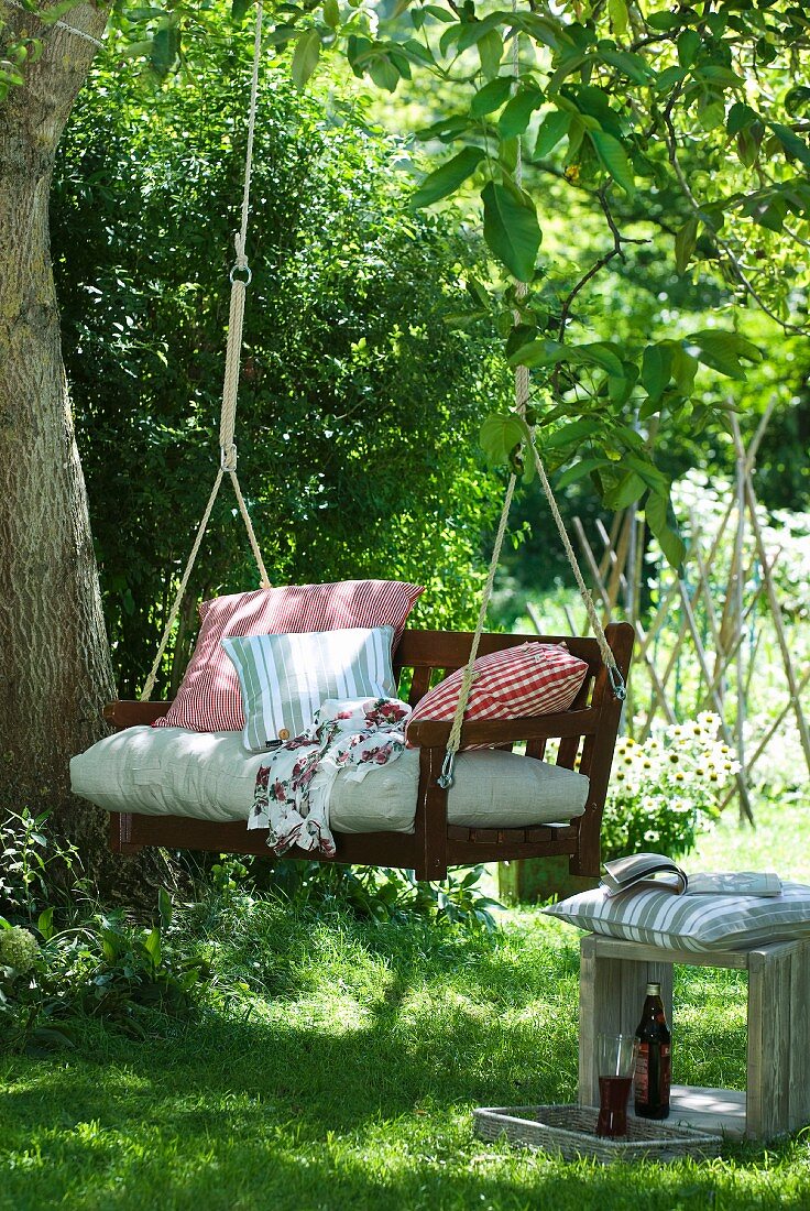 Gartenschaukel aus Holz mit Seilaufhängung und Kissen unter einem Baum