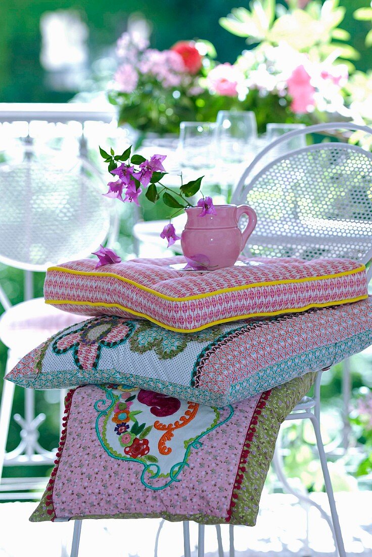 Small jug of bougainvillea flowers and patchwork cushions with complex floral motifs on white metal chair