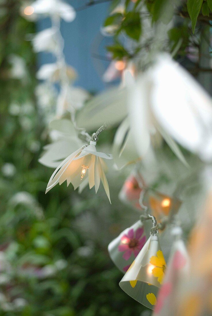 Lighted string of fairy lights with shades shaped like various flowers as decoration for garden party