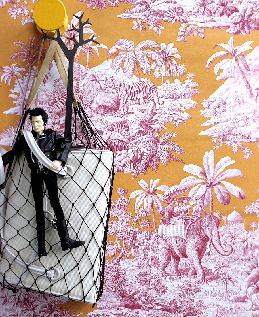 Bag in net and cult action figure against Toile de Jouy wallpaper