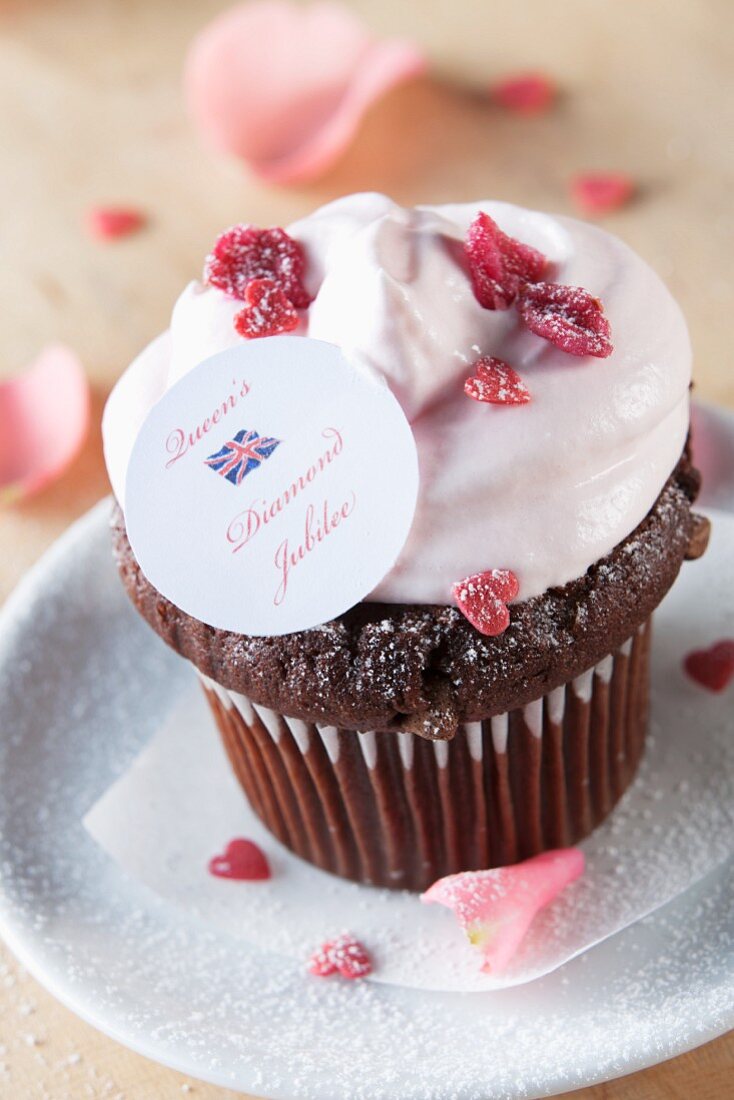 A chocolate cupcake topped with cream, candied rose petals and a Union Jack decoration