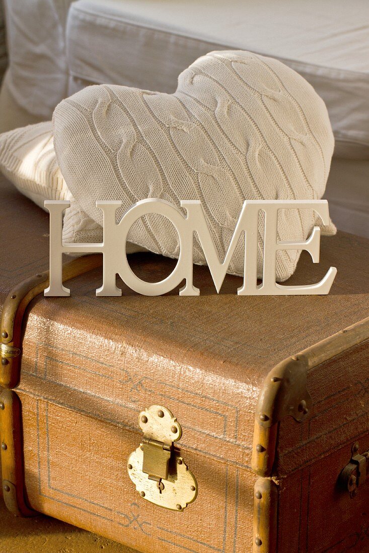 White-painted wooden letters and cushions on old trunk