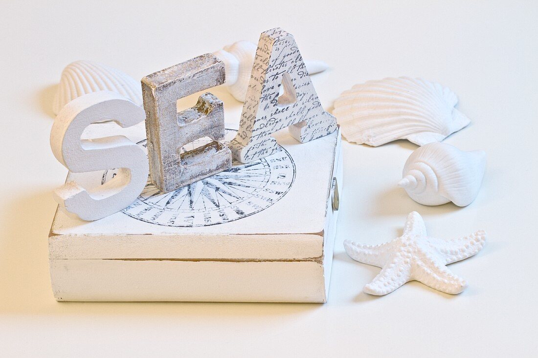 White-painted wooden letters on box surrounding by seashells