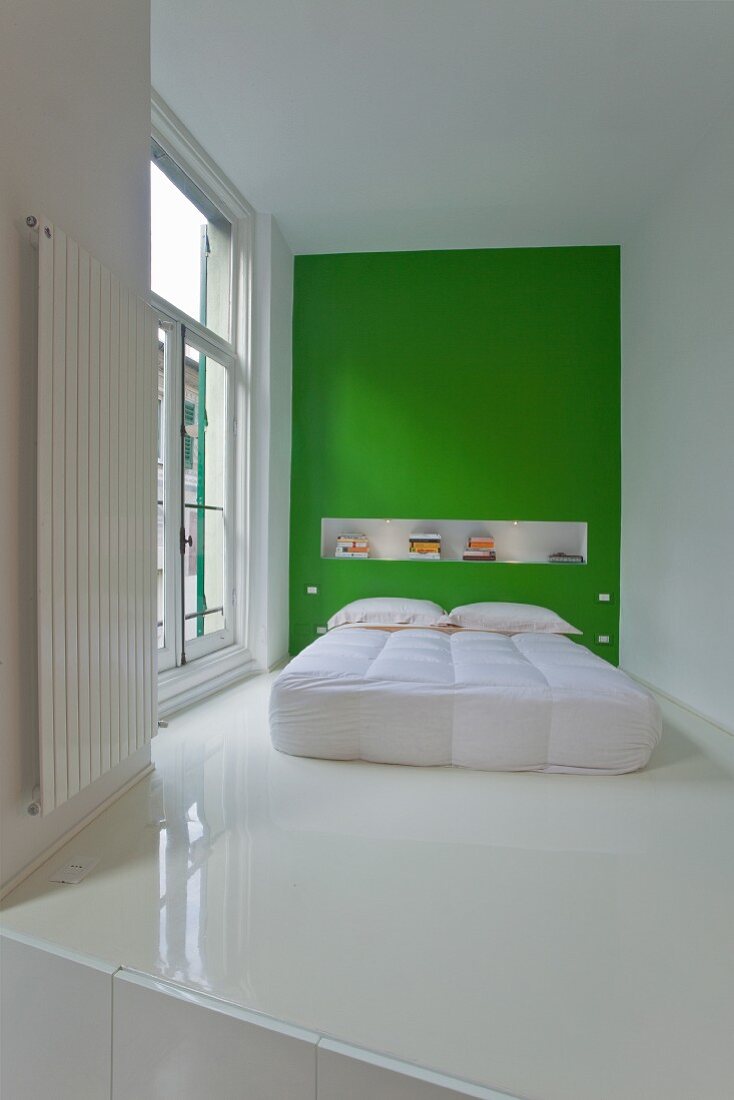 Modern bed with white bedspread against green wall on white epoxy resin floor