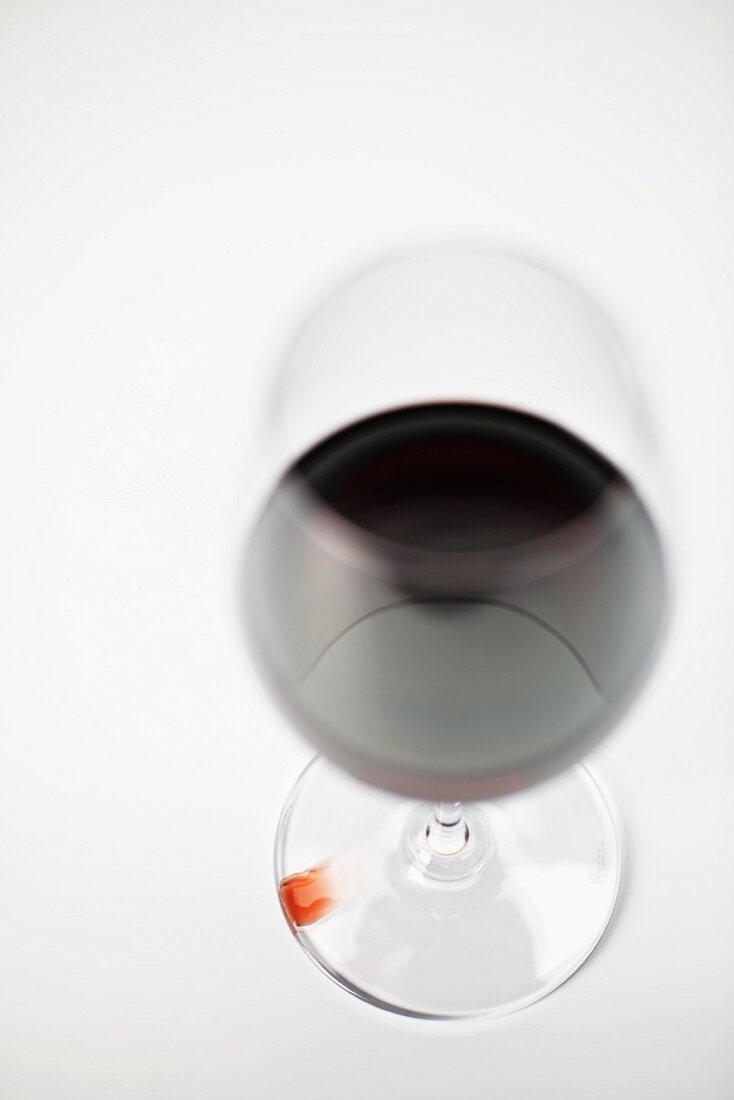 A glass of red wine and a drop of wine on the base of the glass