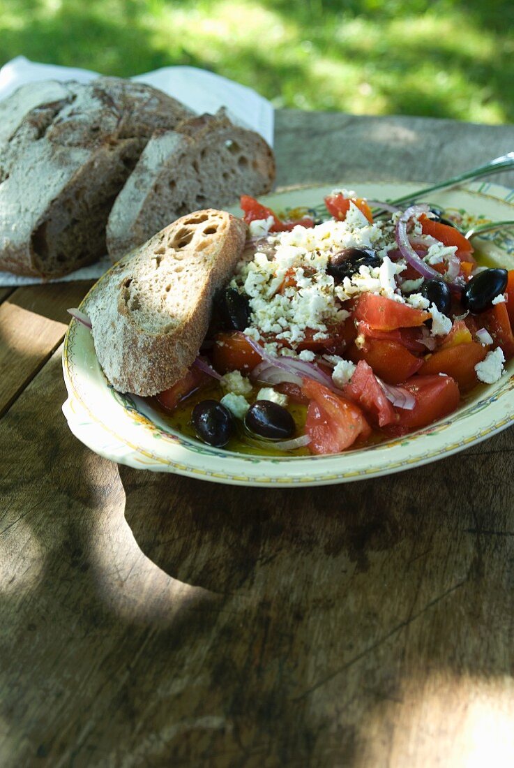 Greek Salad with Feta Cheese, Tomatoes, Olives and Red Onion; With Bread; On Outdoor Table