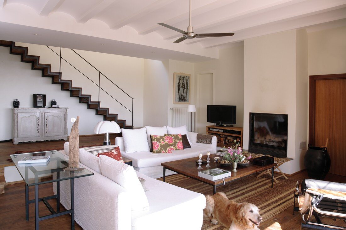 White sofa set below Mediterranean ribbed ceiling with fan and open-plan interior staircase in background