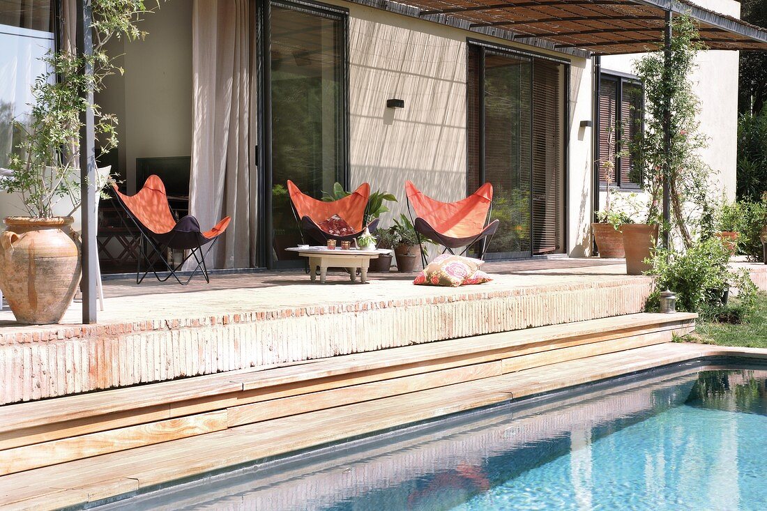 Sitzgruppe mit Fledermaussesseln auf mediterraner Terrasse mit Pergola-Überdachung; Pool-Ausschnitt im Vordergrund