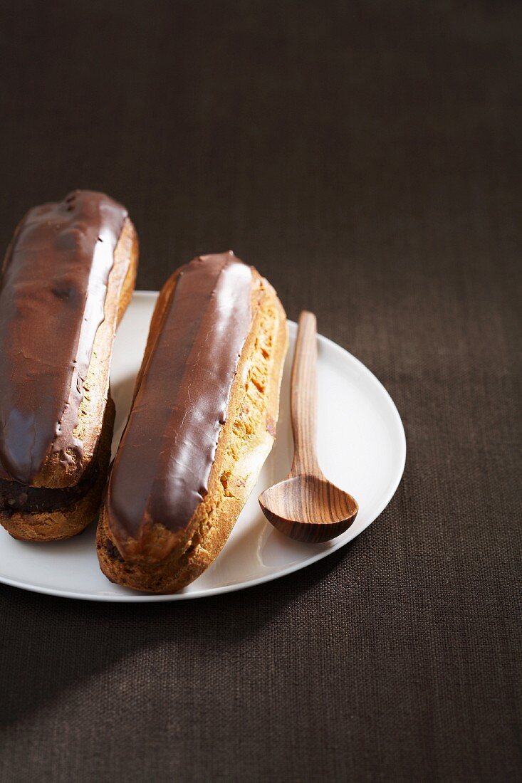 Zwei Schokoladen-Eclairs auf Teller mit Holzlöffel