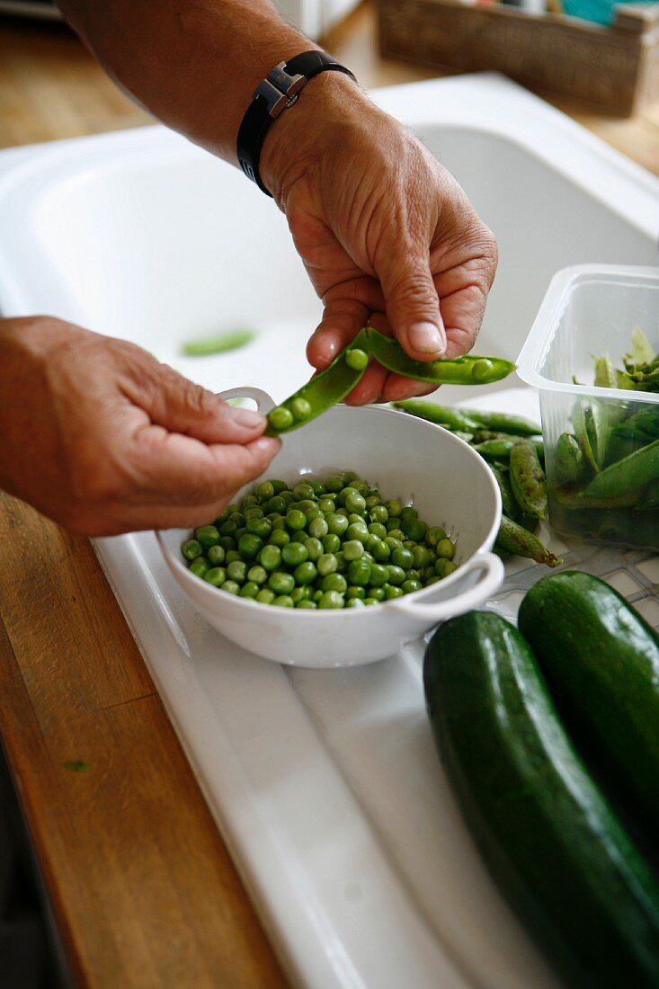 Peas being shelled and vegetables on a work surface