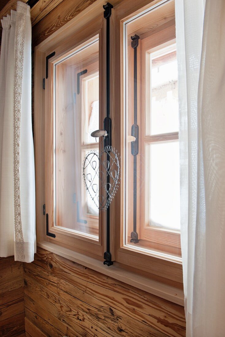 White curtains at window of rustic wooden hut