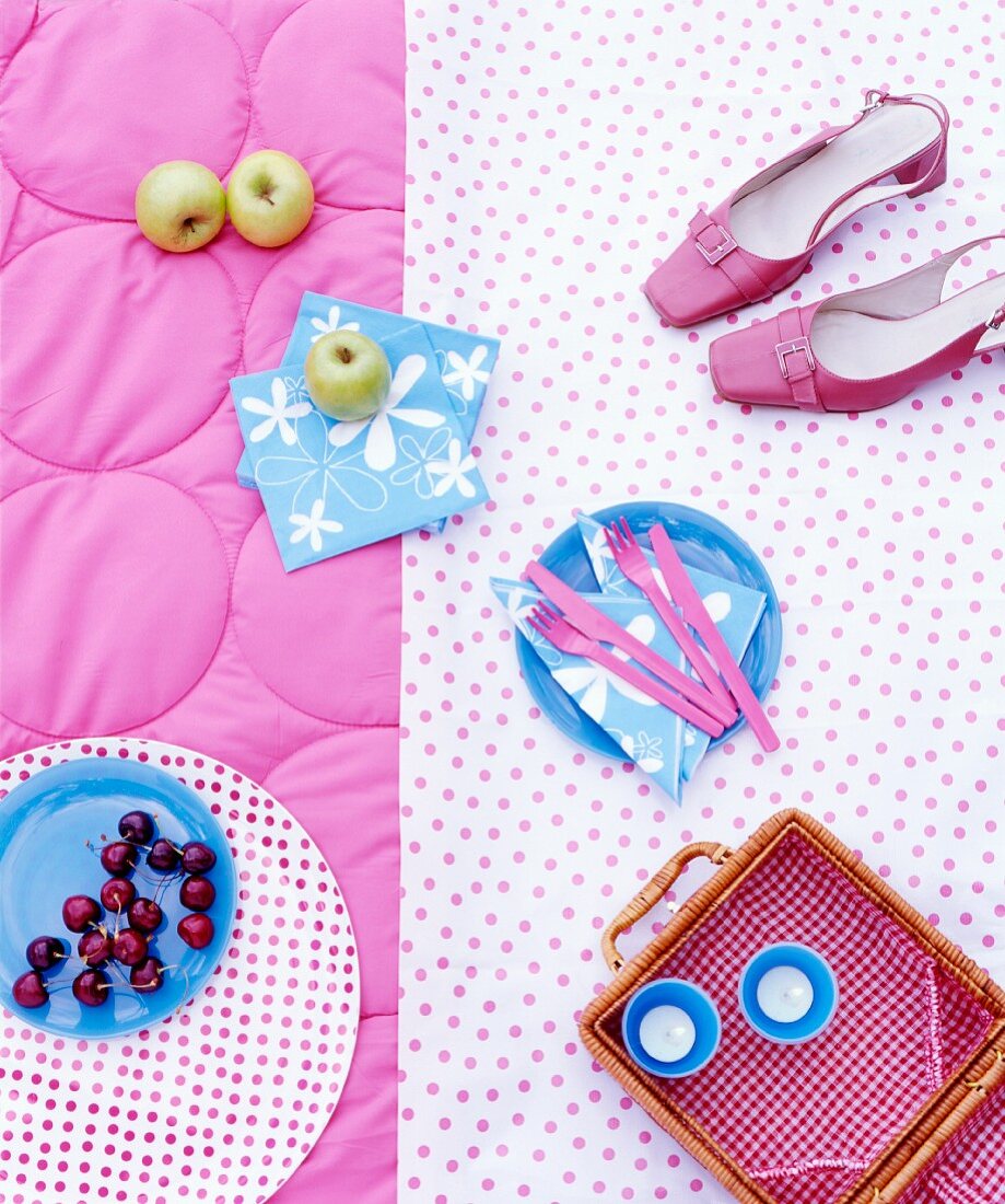 Shoes, cherries, a picnic basket, apples, napkins and cutlery on a picnic blanket