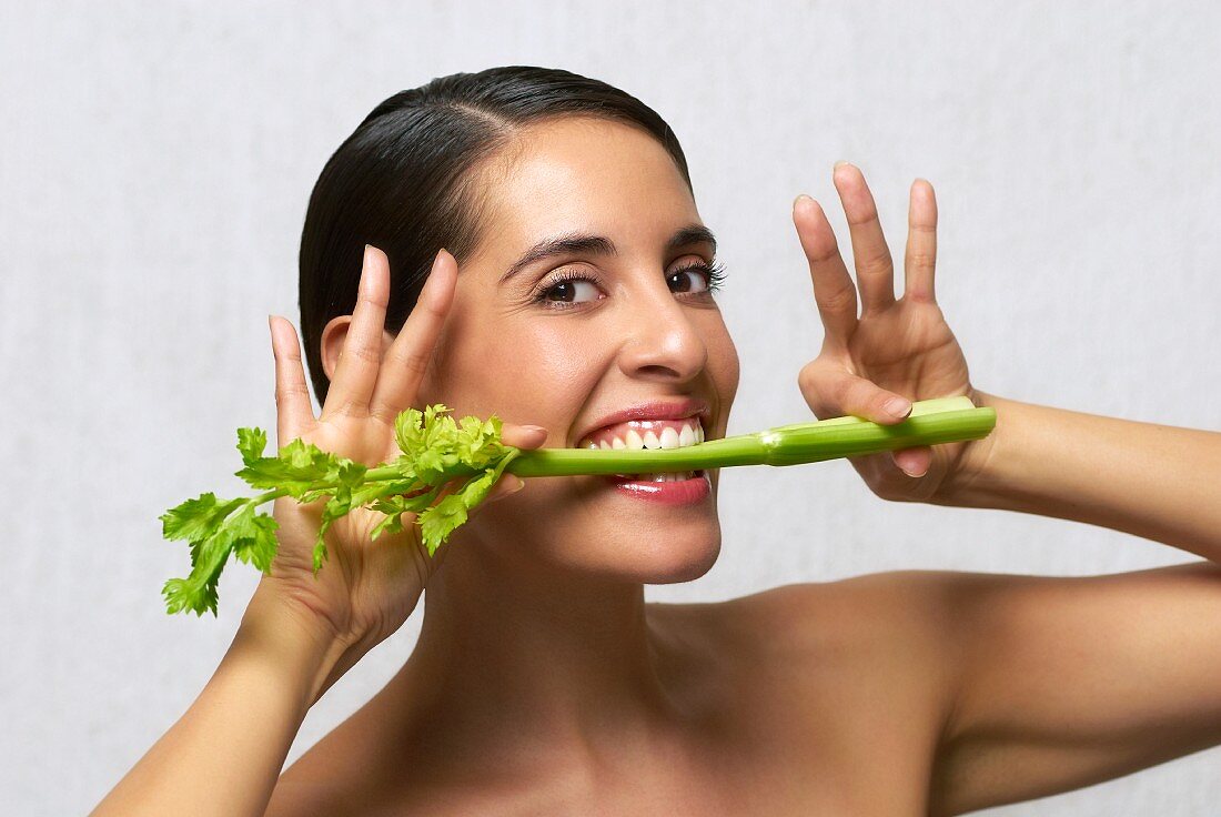 A woman biting into a stick of celery