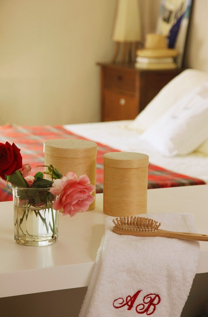 Roses, towel, hairbrush and containers on shelf in bedroom