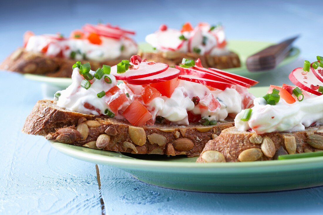 Slices of pumpkin seed bread topped with tomato and radish quark