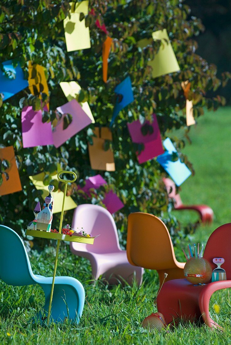 Bunte Plastiksttühle unter einem Baum mit Papierdeko