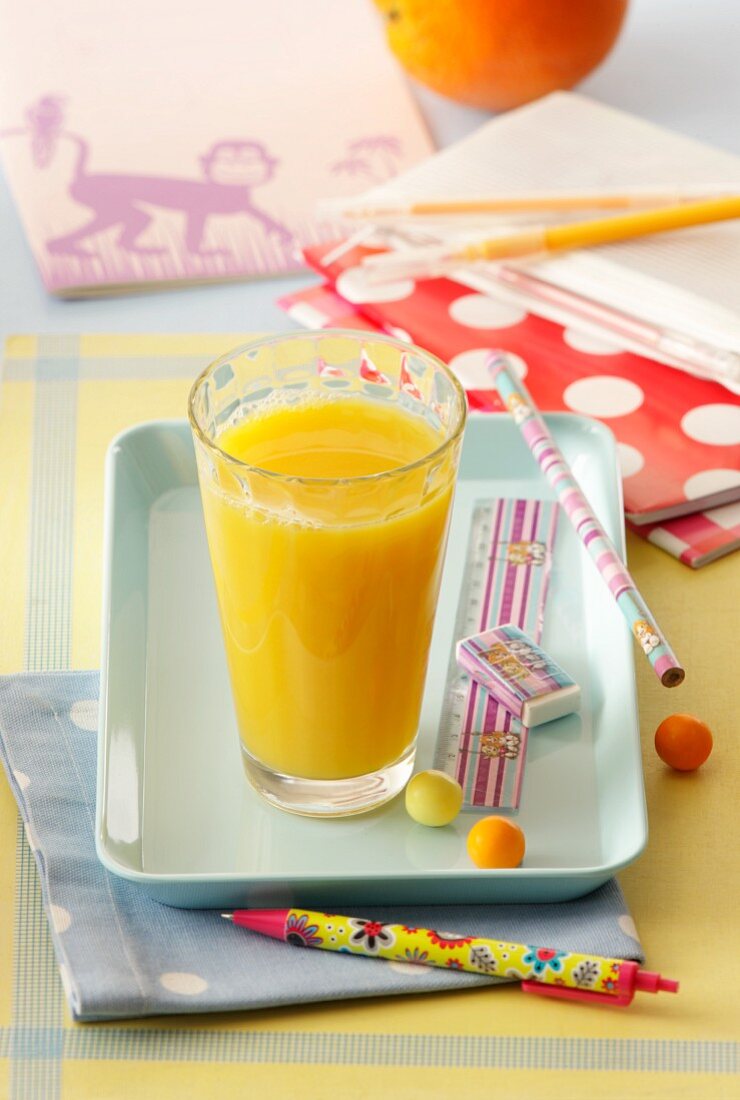 Ein Glas Orangensaft auf Tablett mit Schulsachen