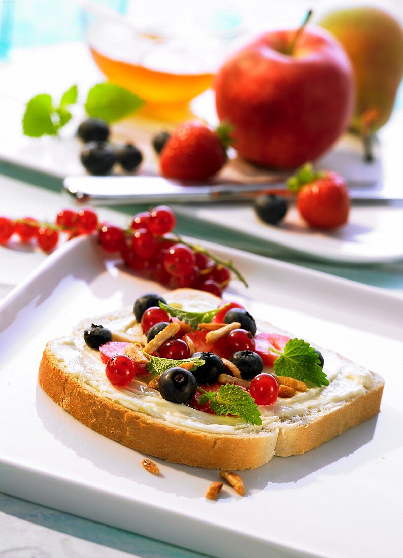 A slice of buttered bread topped with fruit and slivered almonds
