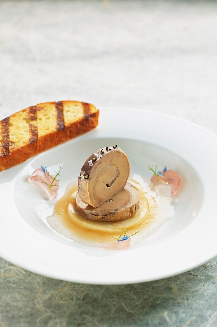 Rolled goose liver terrine on a pool of apple sauce with rose jelly and brioche