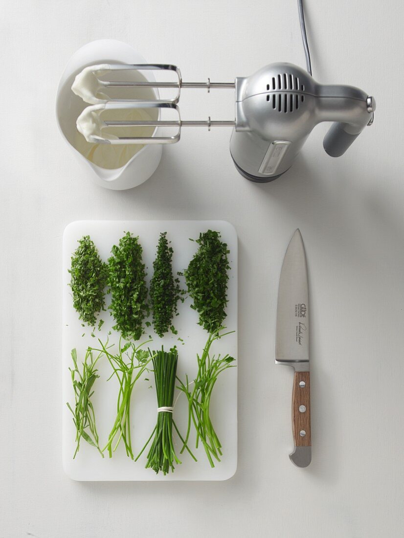 Chopped herbs on a chopping board, whipped cream and a mixer