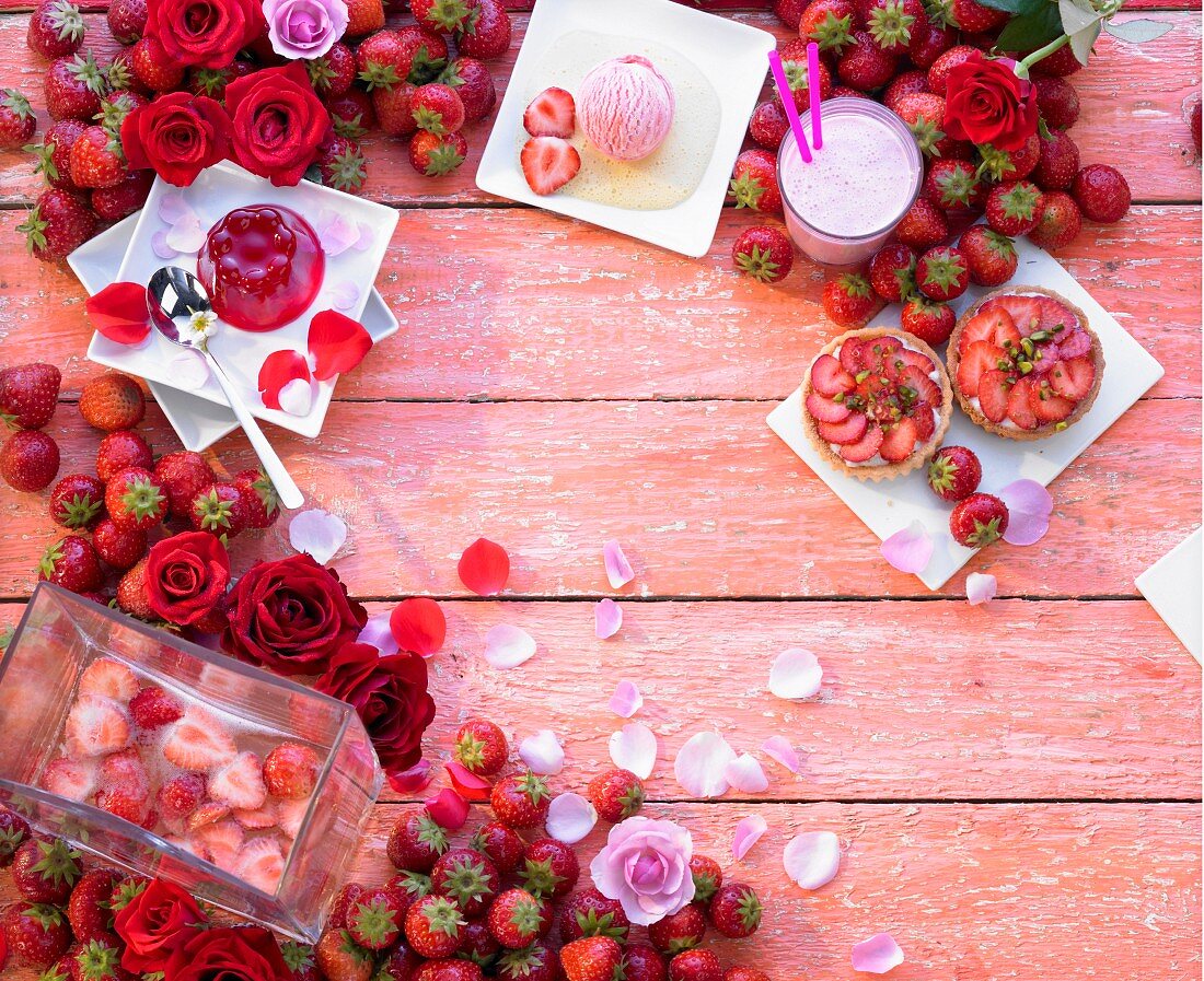 Verschiedene Erdbeerdesserts, frische Erdbeeren und Rosen um den Bildrand