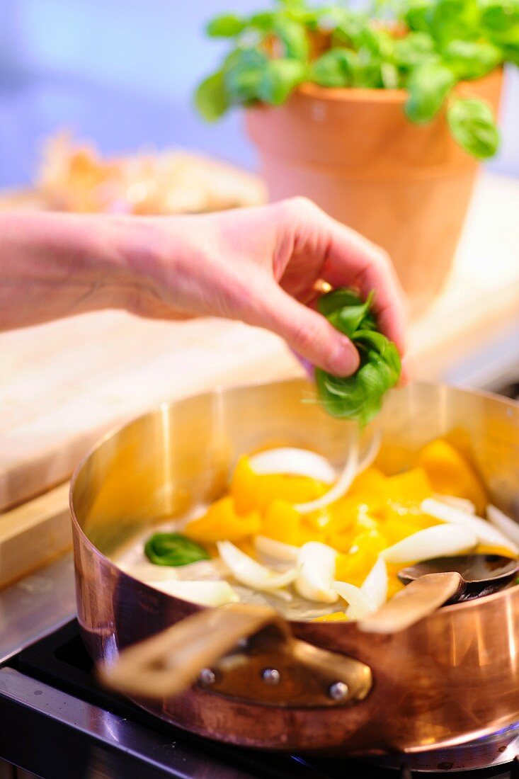 Basil being added to pan of peppers and onions