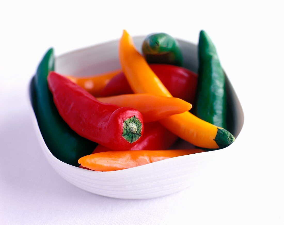 Fresh chilli peppers (red, orange, green) in a bowl