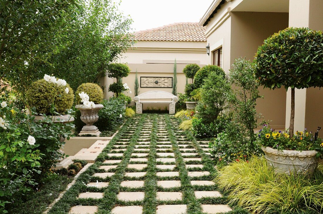 Front garden designed in antique Italian style with ornamental concrete bench at end of paved path