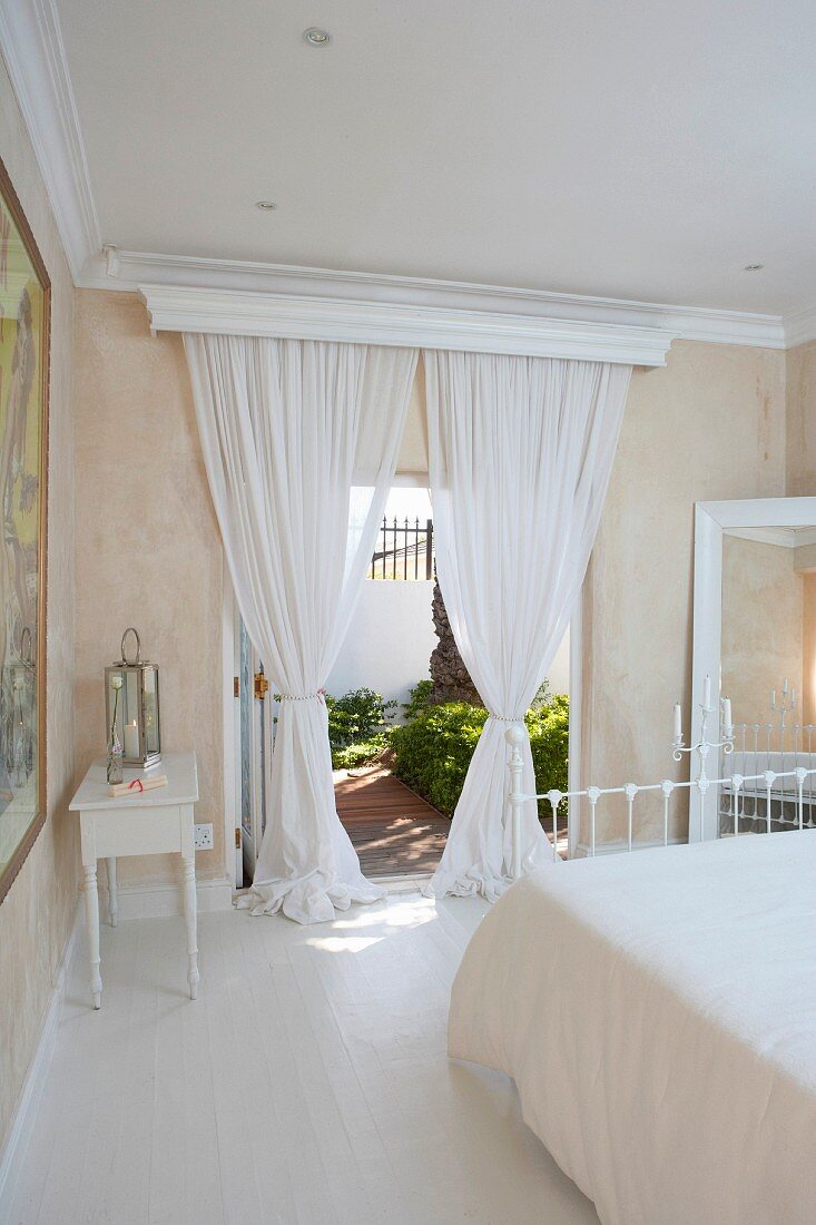 Romantic bedroom in Mediterranean villa - white, airy curtains at open terrace doors