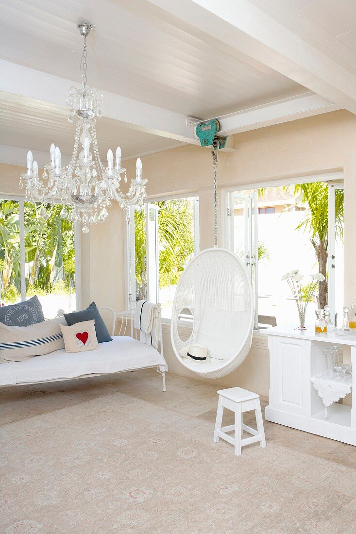 White, Mediterranean interior - wicker chair hanging from ceiling next to sideboard with bar and bench with white metal frame