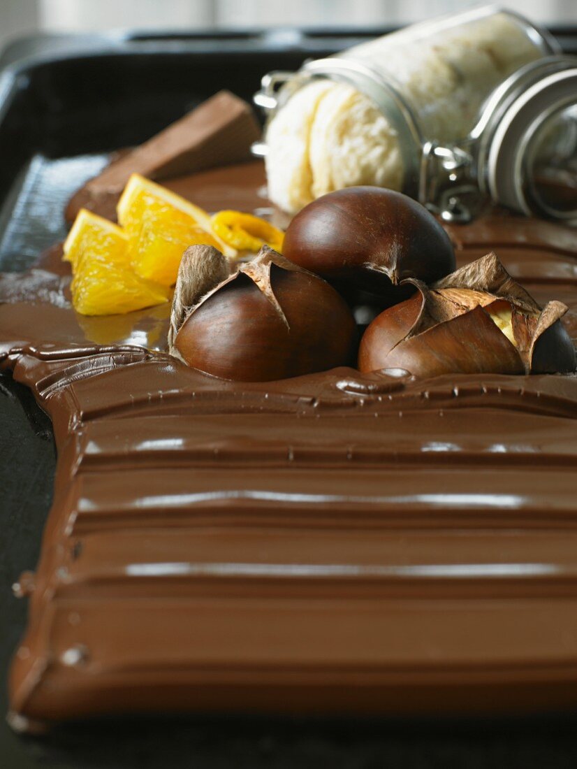 Stillleben mit angeschmolzener Schokolade, Maroni und Orange