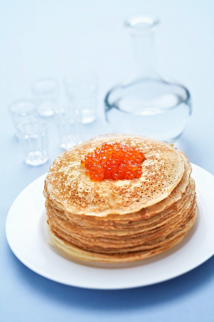 A stack of blinis with salmon caviar and vodka