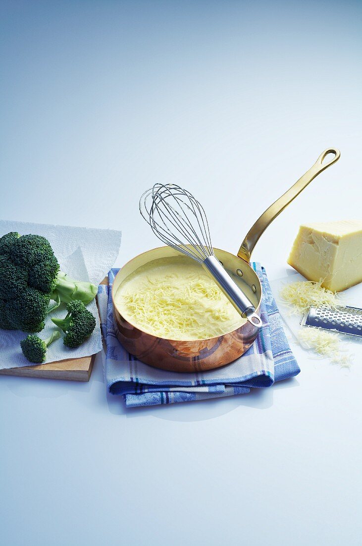 Cheese sauce in a copper pan, broccoli and a piece of cheese