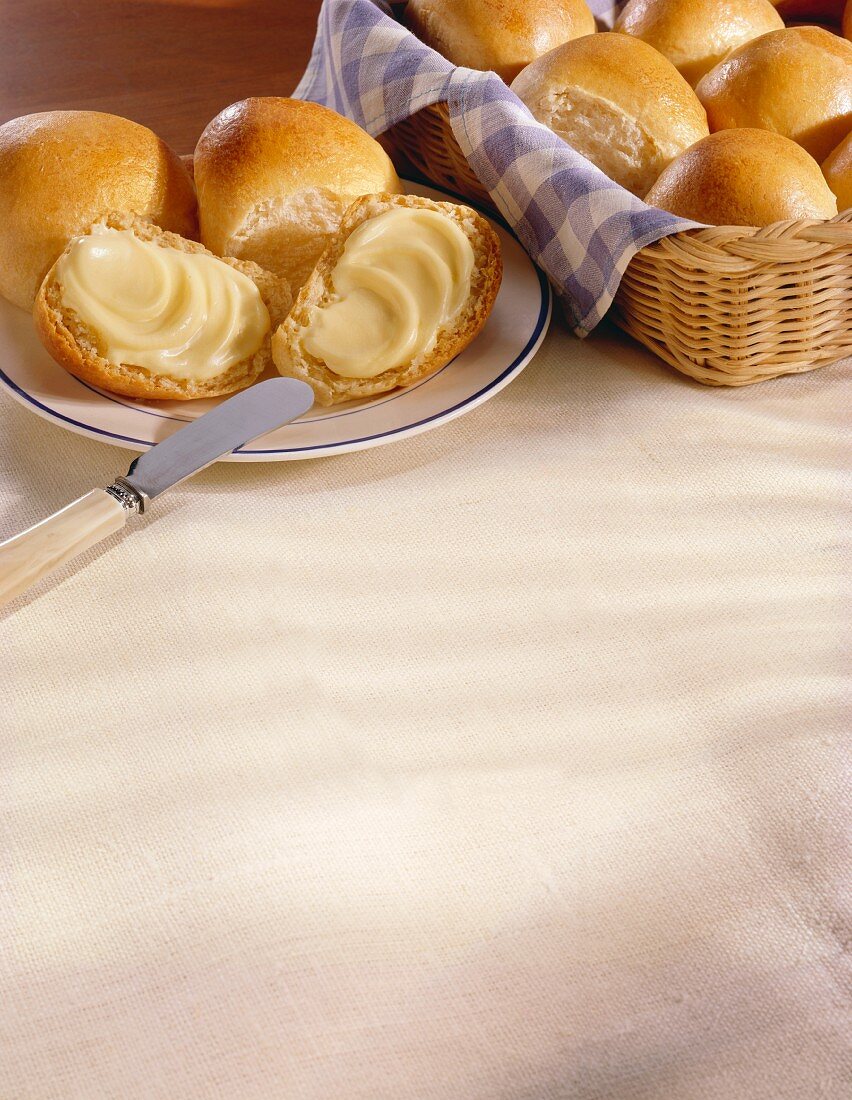 Dinner Rolls in a Basket; Some on a Plate with Butter
