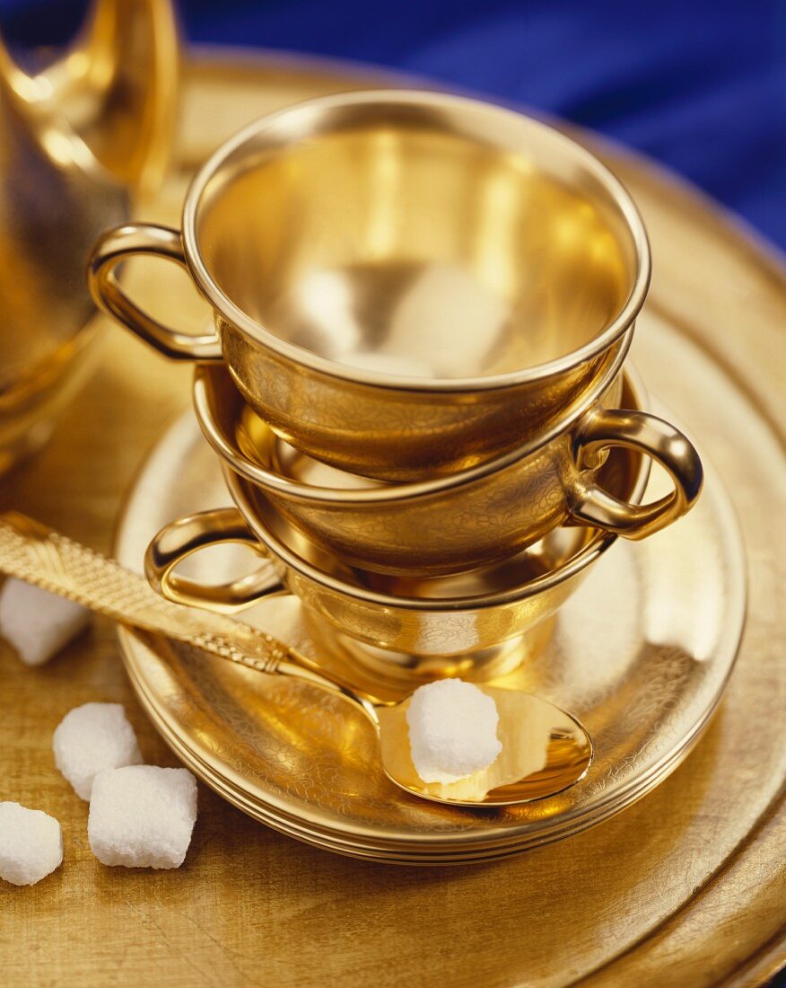 Goldene Teetassen, Löffel und Zuckerwürfel