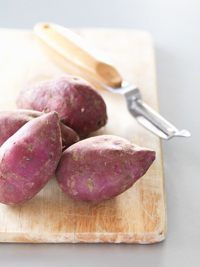 Sweet potatoes on a chopping board with a peeler