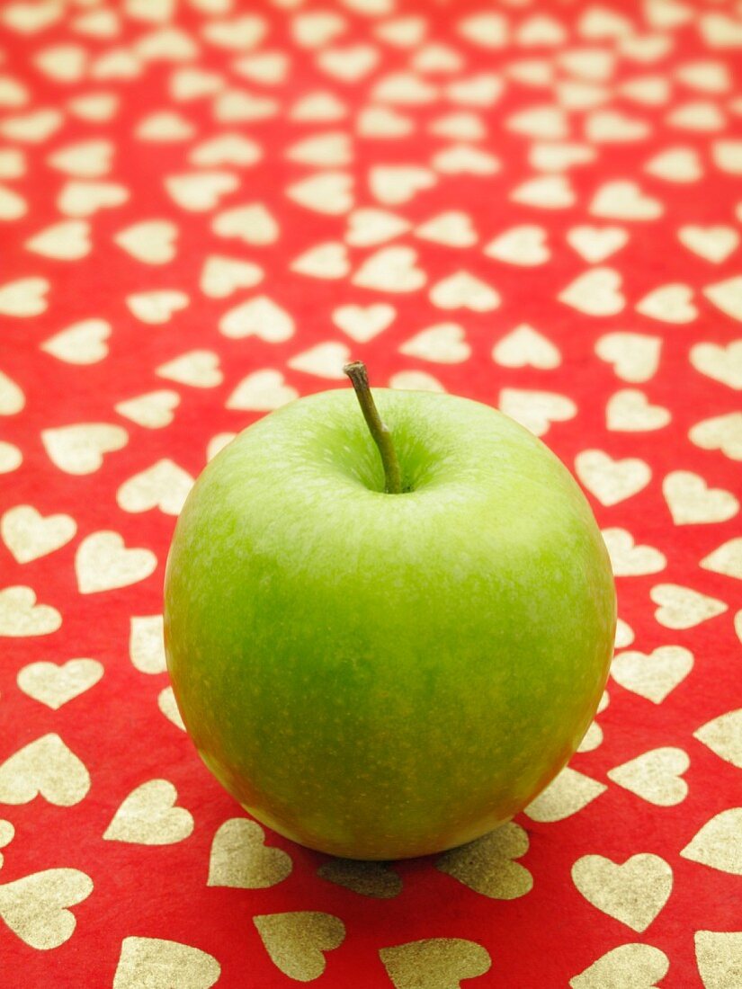 A green apples on a red surface patterned with hearts