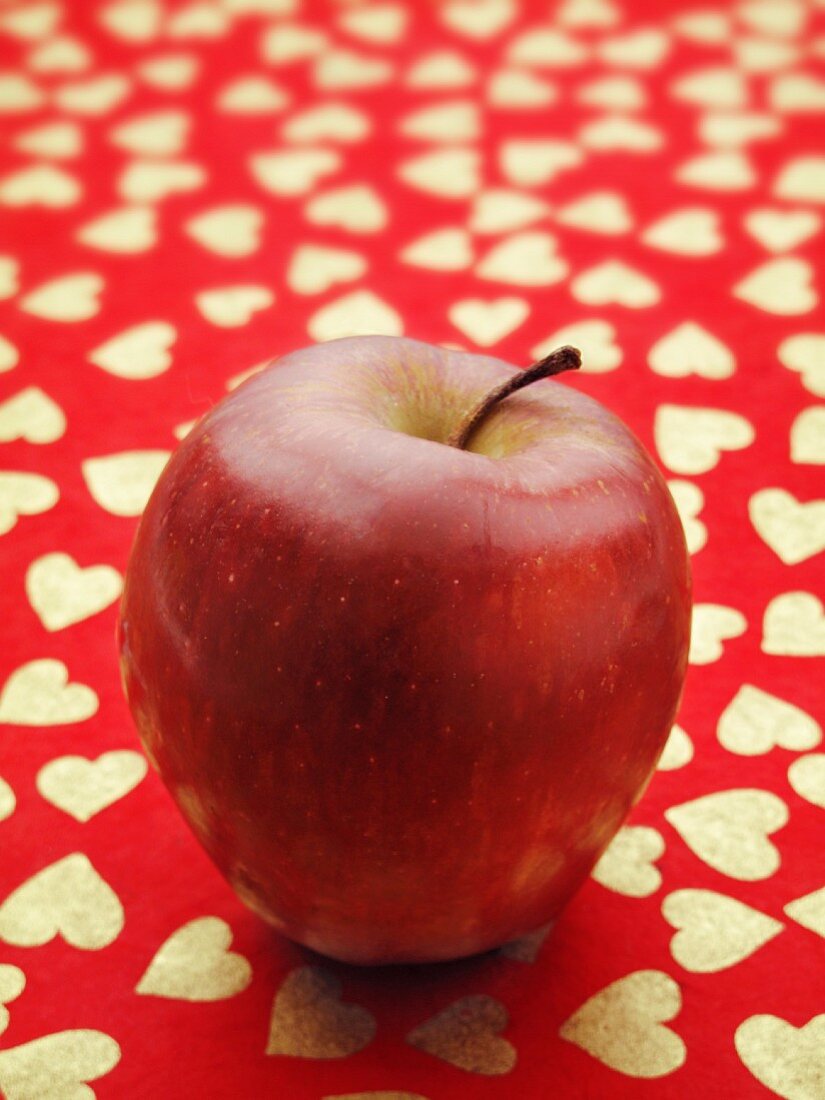 Ein roter Apfel auf rotem Untergrund mit Herzdeko