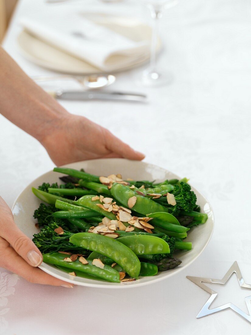 A woman serving a plate of vegetables with slivered almonds (Christmas)