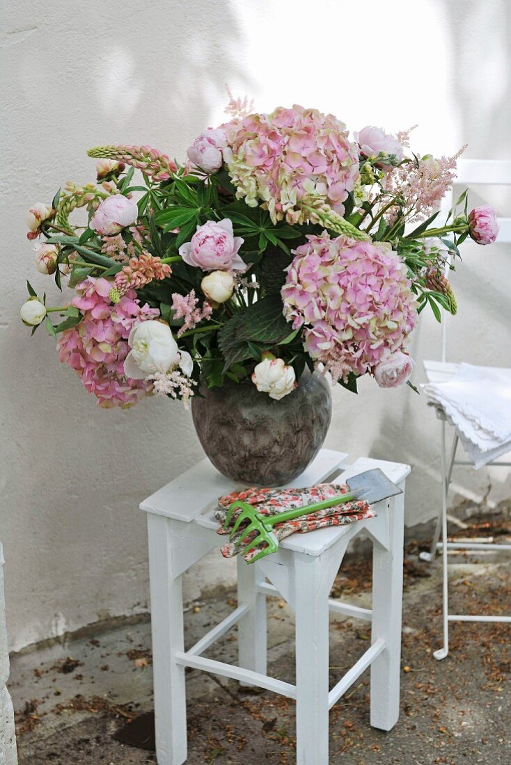 Bouquet of hydrangeas in vase on white-painted stool against exterior wall